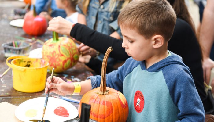 A little boy painting a small pumpkin.