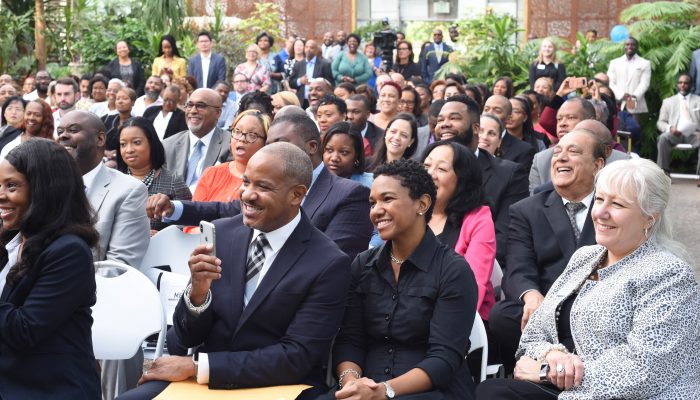 Attendees at the Minority Enterprise Development Week Kickoff Breakfast and Awards Ceremony are seated in row chairs while smiling and celebrating.