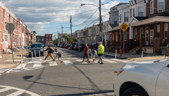 A family crossing a residential street with a crossing guard