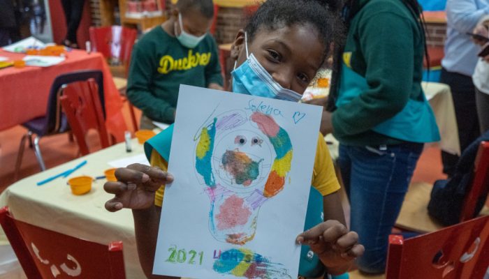 An African-American girl holds up a picture of her Lights On Afterschool lightbulb.