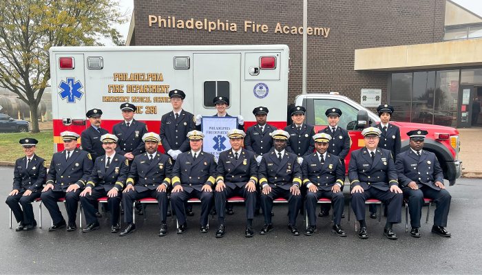 paramedics and firefighters in dress uniforms sitting and standing in alongside ambulance for formal class portrait