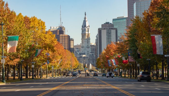 philadelphia city hall in the background from the vantage point of of the ben franklin parkway with trees with fall foliage lining the street