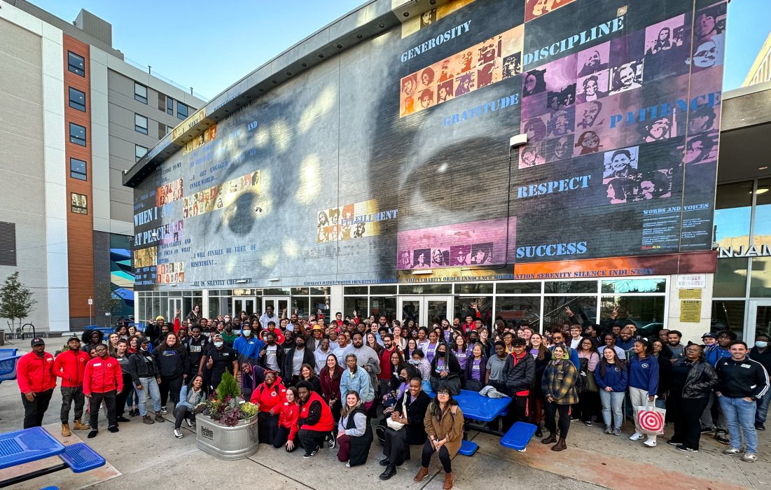 AmeriCorps members from various programs gather at the 2022 AmeriCorps Launch in front of a muraled building.