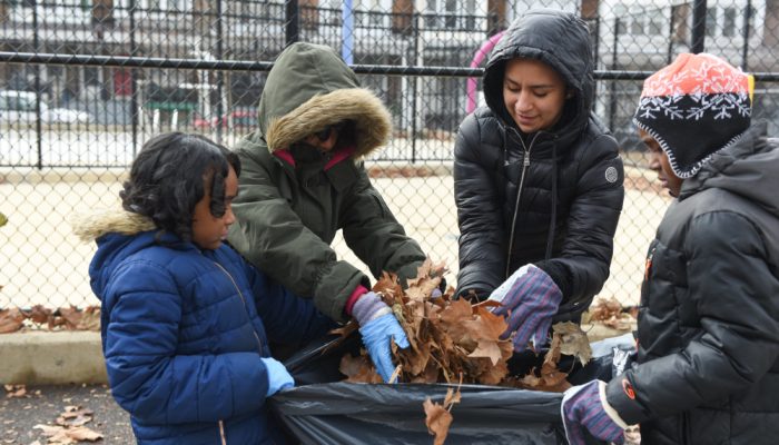 Kids putting piles leaves in trash bag.