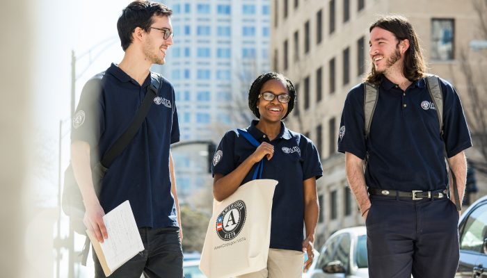 Three VISTA members wearing branded navy blue polos walk down a city street while talking.