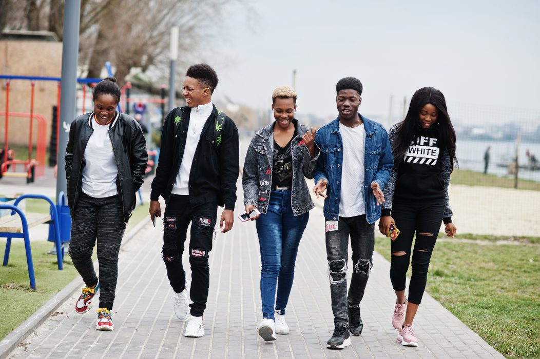 Teenage friends in jeans and casual clothing talk and laugh while they walk down a street