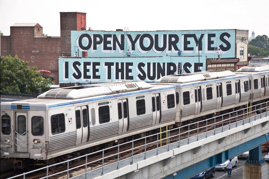 a septa market frankford line train passes in front of a mural on the side of a building that says open your eyes I see the sunrise