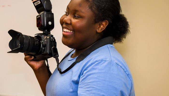 Una joven afroamericana con una cámara y sonriendo.