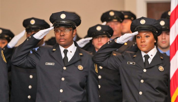 cadets in dress uniforms and white gloves saluting at graduation