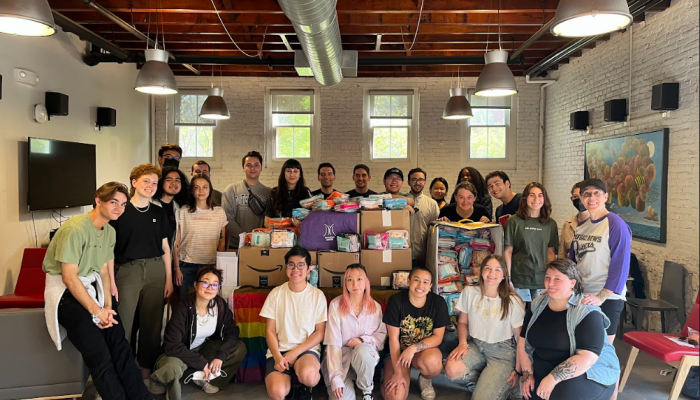 20+ Mazzoni Center volunteers pose for a photo around a table filled with boxes they've packed for distribution.