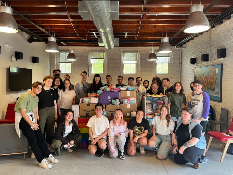 20+ Mazzoni Center volunteers pose for a photo around a table filled with boxes they've packed for distribution.
