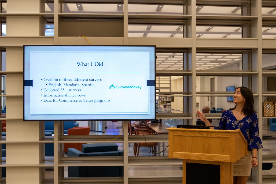 A VISTA members stands behind a podium and points to a screen to displaying their Lightning Talks presentation.