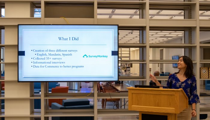 A VISTA members stands behind a podium and points to a screen to displaying their Lightning Talks presentation.