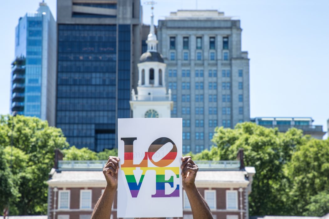 Poster with the word LOVE in rainbow colors, held up in front of Independence Hall