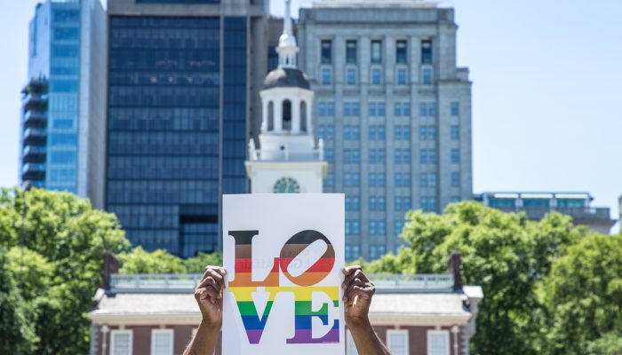 Poster with the word LOVE in rainbow colors, held up in front of Independence Hall