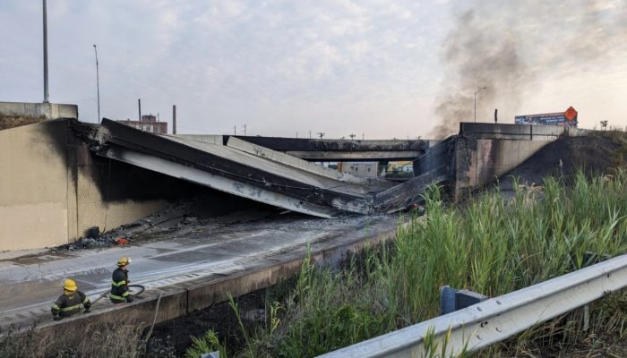 a section of I-95 that is collapsed with smoke coming out from under the rubble. Emergency personnel are in the bottom left hand corner