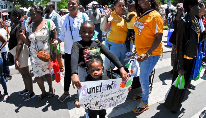 Children are holding a sign that reads Juneteenth Let Freedom Ring. They are in a crowd and are participating in the Juneteenth Parade.