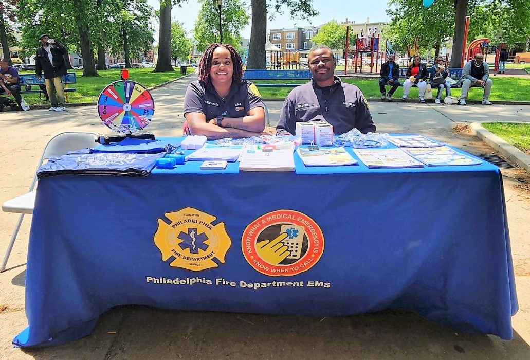 female and male paramedics sitting in park behind table filled with health resources and narcan