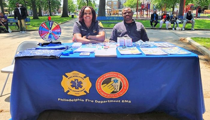 female and male paramedics sitting in park behind table filled with health resources and narcan