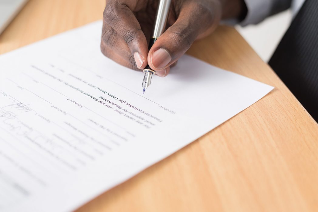 A person signs a paper contract on a wood table