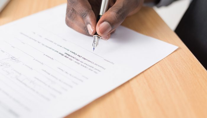 A person signs a paper contract on a wood table