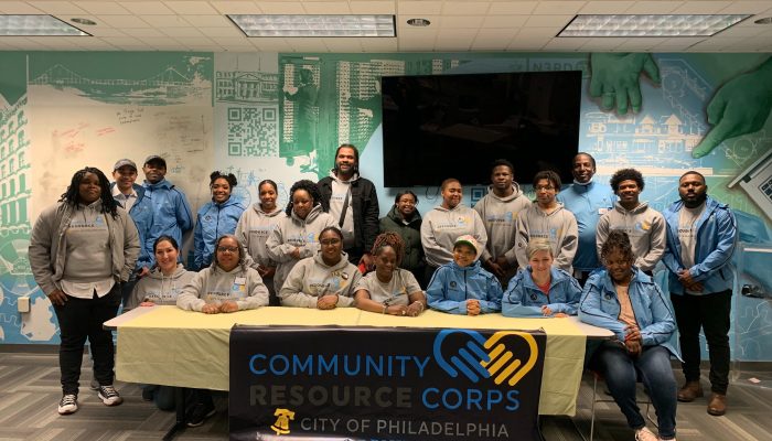 Los miembros del Community Resource Corps visten ropa de marca y están sentados o de pie detrás de una mesa con un mantel de la marca CRC.