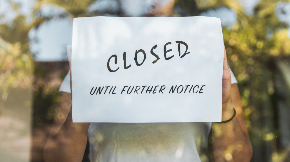 A store associate holds Closed until further notice sign