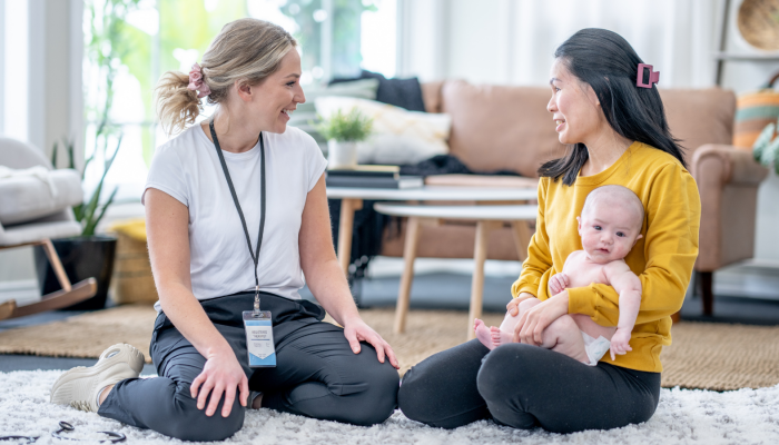 A social worker sits on a rug with a new mom and her baby.