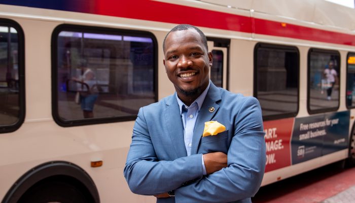 Raheem Manning smiling and crossing his arms in front of his chest with a SEPTA bus driving by in the background