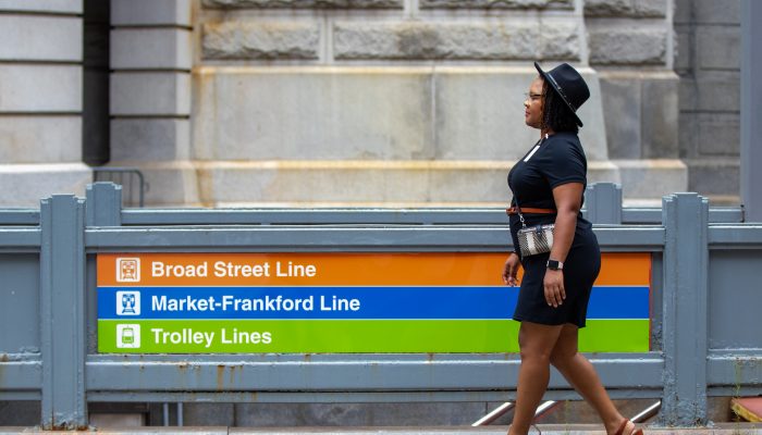Samaria Brandon walking past a SEPTA entrance with a sign on it that says Broad Street Line, Market-Frankford Line, Trolley Lines
