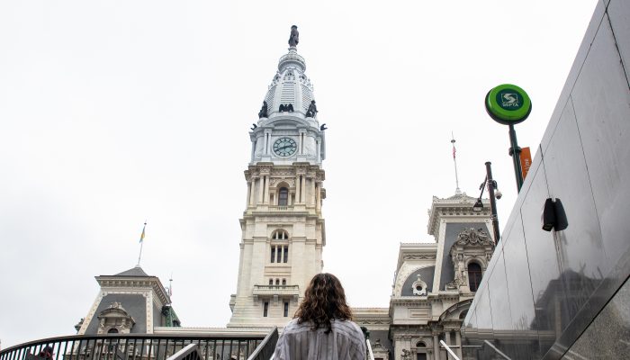 Aikaterini Papazoglou walking up a stairway with Philadelphia City Hall in the background and a SEPTA sign
