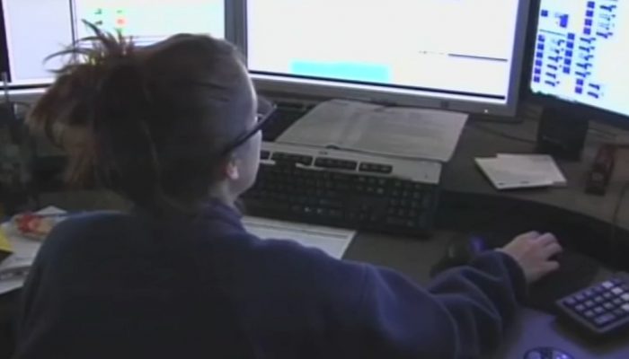 A call-taker sits at a desk in front of three computer screens