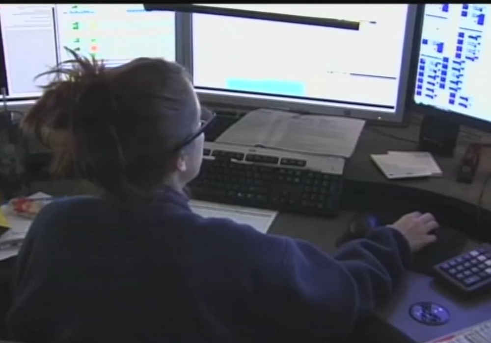 A call-taker sits at a desk in front of three computer screens