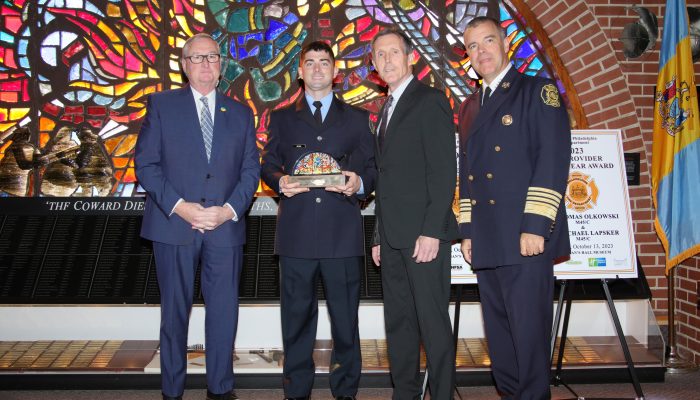 firefighter in dress uniform holds award while standing with three men in front of stained glass window