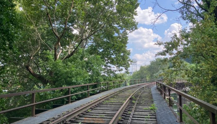 Uma foto tirada da Mule Bridge em um dia de verão. Um único trilho para um trem em primeiro plano se estende até o horizonte, longe da perspectiva do fotógrafo.