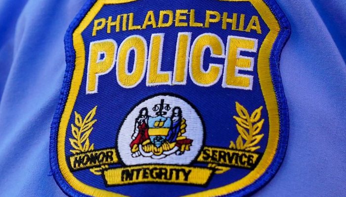 Un écusson bleu foncé de la Police de Philadelphie orné de lettres jaunes se trouve sur le dessus d'une manche de chemise bleu clair