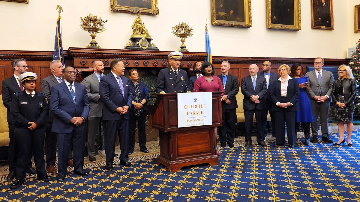 Several people standing in an ornate room at city hall. New Acting Fire Commissioner Craig Murphy stands at the podium.