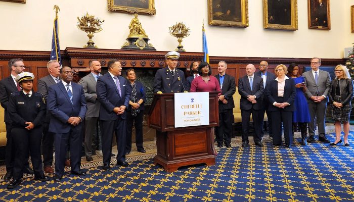 Several people standing in an ornate room at city hall. New Acting Fire Commissioner Craig Murphy stands at the podium.