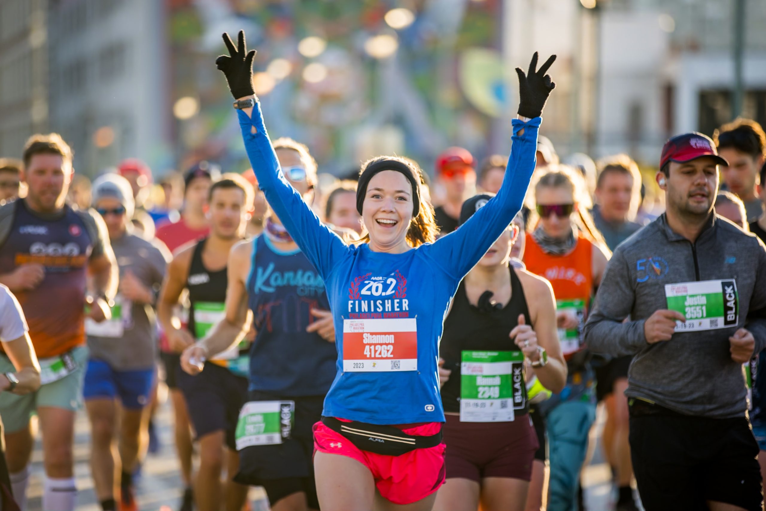 A runner triumphantly throws their hands in the air as they run in the Philadelphia Marathon