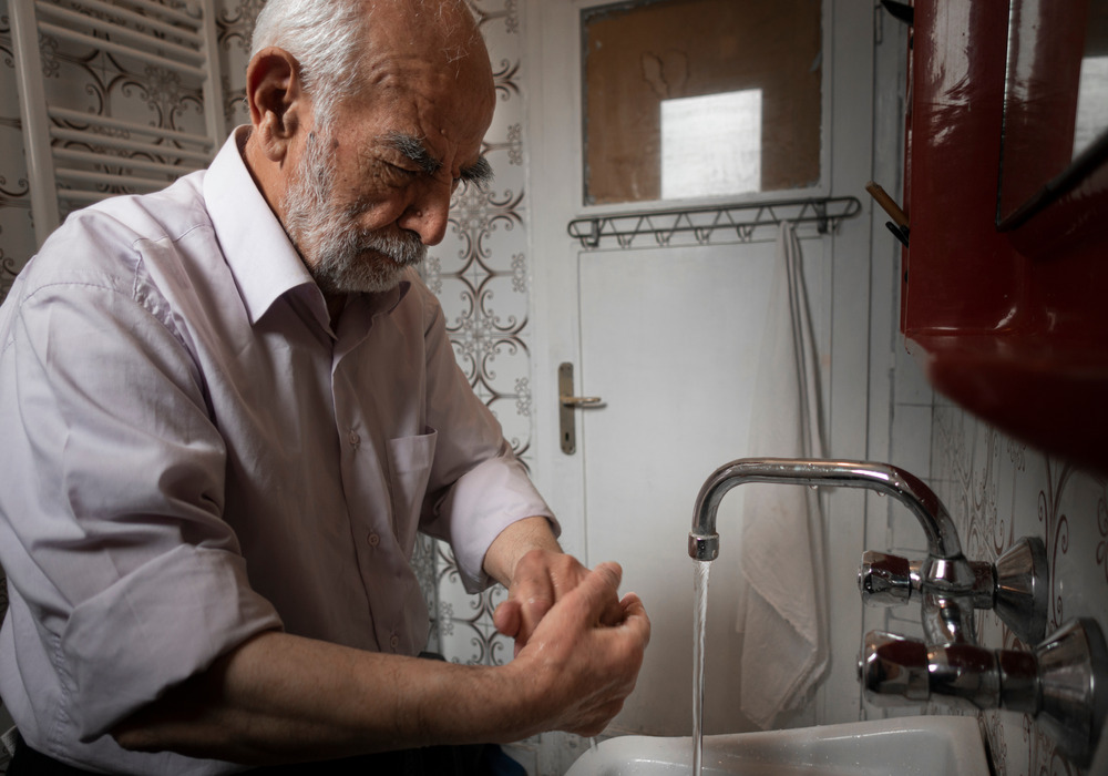 An older man washes his hands in kitchen sink