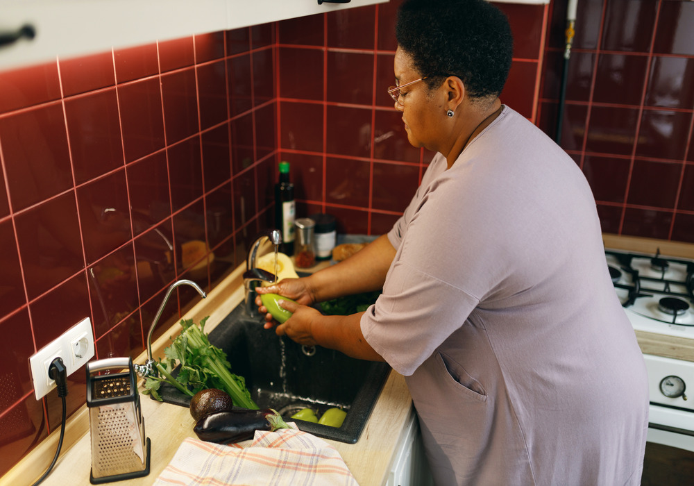 An older woman washes veggies in the sink