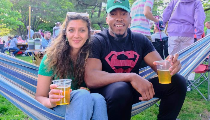 A couple sit on a hammock and relax while drinking beer.