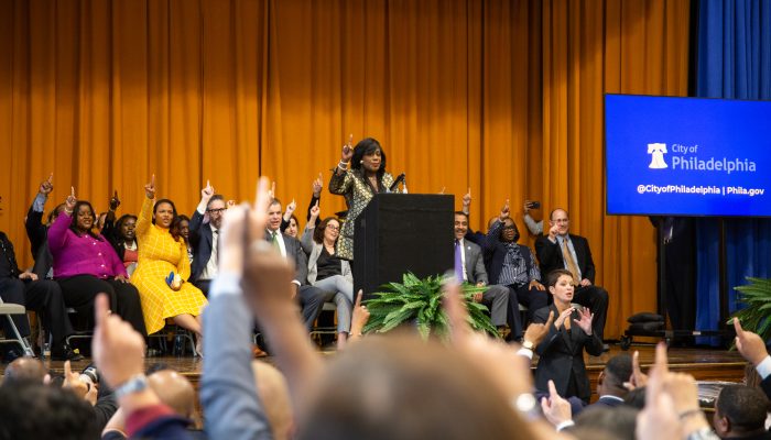 Image of Mayor Parker on a stage with members of her Administration holding their pointer fingers in the air