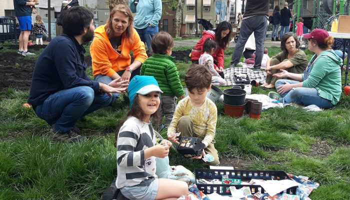 Children and parents decorate pots on the lawn in the park on Earth Day. The children are putting stickers on the pots. They are also burying plant seeds.