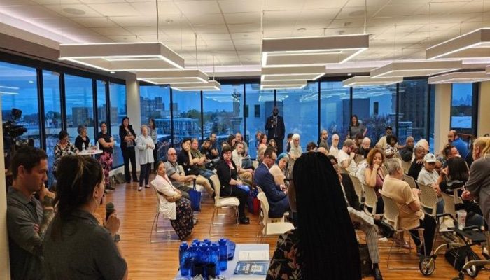 A conference room filled with people in seats listening to speakers.