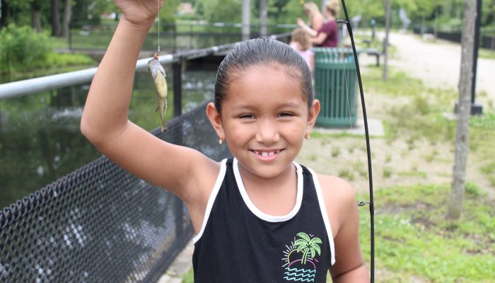 A young hispanic girl smiles while holding up the fish she caught on one of Philadelphia Parks & Recreation's free fishing programs.