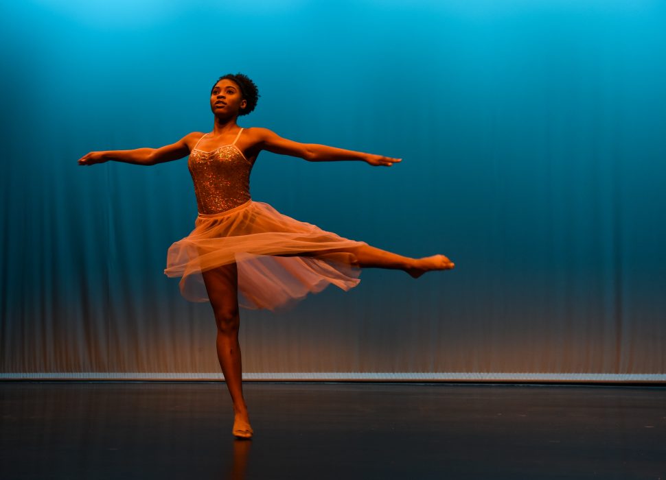 A young woman in ballet attire performs on stage.