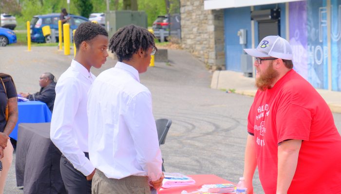 Deux jeunes en costume discutent avec un recruteur lors d'un salon de l'emploi.