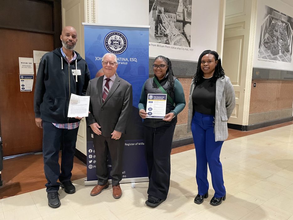 Mr. Henderson standing next to the Register of Wills holding a deed transfer, following his wife, Mrs. Henderson and TCU Director, Myasia Williams. They are standing in front of the Register of Wills sign.