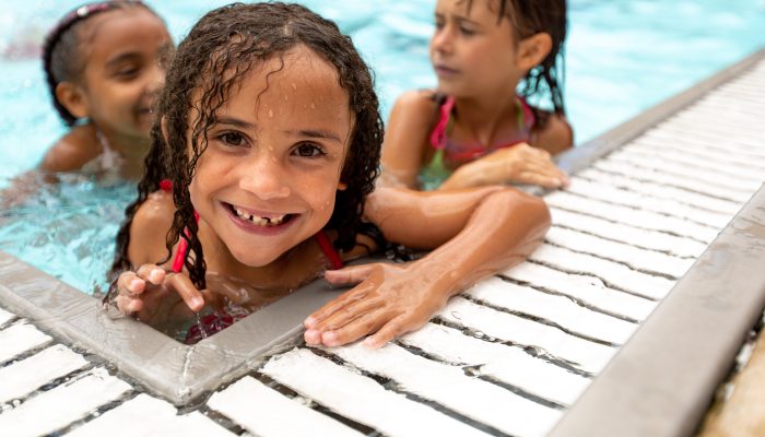 Three young children smile while swimming in the public pool.